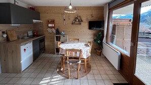 Une cuisine chaleureuse avec une table à manger, des meubles de rangement en bois et une grande fenêtre donnant sur une vue imprenable sur les montagnes.