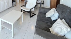 Un salon moderne avec un canapé gris, des coussins blancs et une table basse blanche.