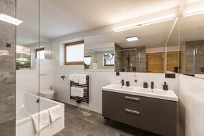 A modern bathroom with a glass-enclosed shower, a vanity with a sink and mirror, and a toilet. - Apartment in Tyrol on the Ski-slope (Lermoos)