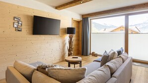 Un salon moderne avec un grand téléviseur à écran plat fixé sur un mur en bois, un canapé avec des coussins, une petite table ronde et une lampe.