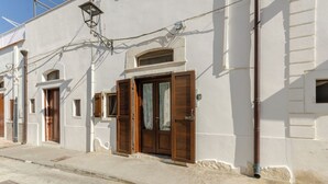 A building with a white facade, wooden doors, and a small window. - Little House in the Junno (Mattinata)