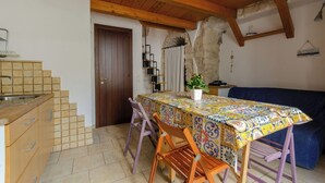 A cozy kitchen with a tiled backsplash, wooden cabinets, and a dining table with colorful tablecloth. - Little House in the Junno (Mattinata)
