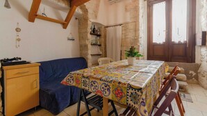 A cozy room with a wooden ceiling, a blue sofa, a table with a colorful tablecloth, and a wooden cabinet. - Little House in the Junno (Mattinata)
