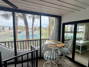 A balcony with a table and chairs, a view of a tennis court, and a building in the background. - Waterfront Cabana Unit in Popular Anglers Cove-Check it Out ! (Marco Island)