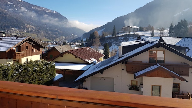 Un village de montagne aux maisons traditionnelles en bois, sous un ciel dégagé, avec des sommets enneigés.