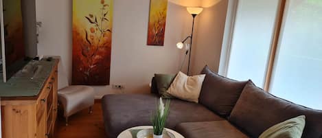 A cozy living room with a brown sofa, a small round table with a plant, and artwork on the walls.