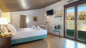 A bedroom with a bed, a desk, a chair, a TV, and a view of the outdoors. - Villa Ariadni Agia pelagia close to the beach up to7-8 quests (Agia Pelagia)