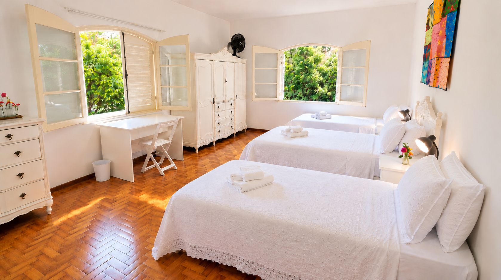 Quarto de hotel com duas camas, uma escrivaninha e um guarda-roupa.