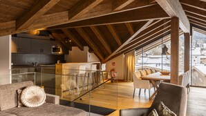 Amplio loft con techo alto, vigas de madera, cocina, comedor y grandes ventanales con vistas al exterior.