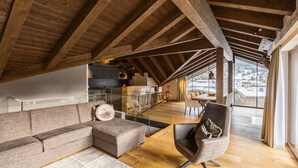 Un loft espacioso con techo alto y vigas de madera a la vista, un sofá modular grande, un sillón moderno y vistas a un paisaje nevado a través de amplias ventanas.