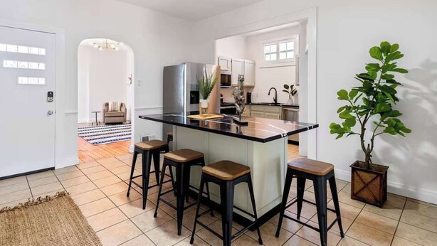 Une cuisine moderne avec un îlot central, des tabourets de bar et une plante en pot.