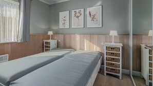 A room with two beds, a window with curtains, and wall-mounted artwork.