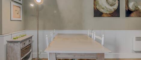 A dining area with a wooden table, white chairs, a floor lamp, and wall art.
