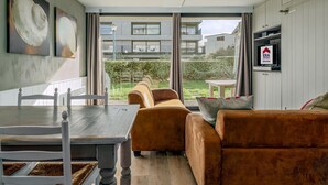 A modern living room with a sofa, a dining table, and a TV mounted on the wall.
