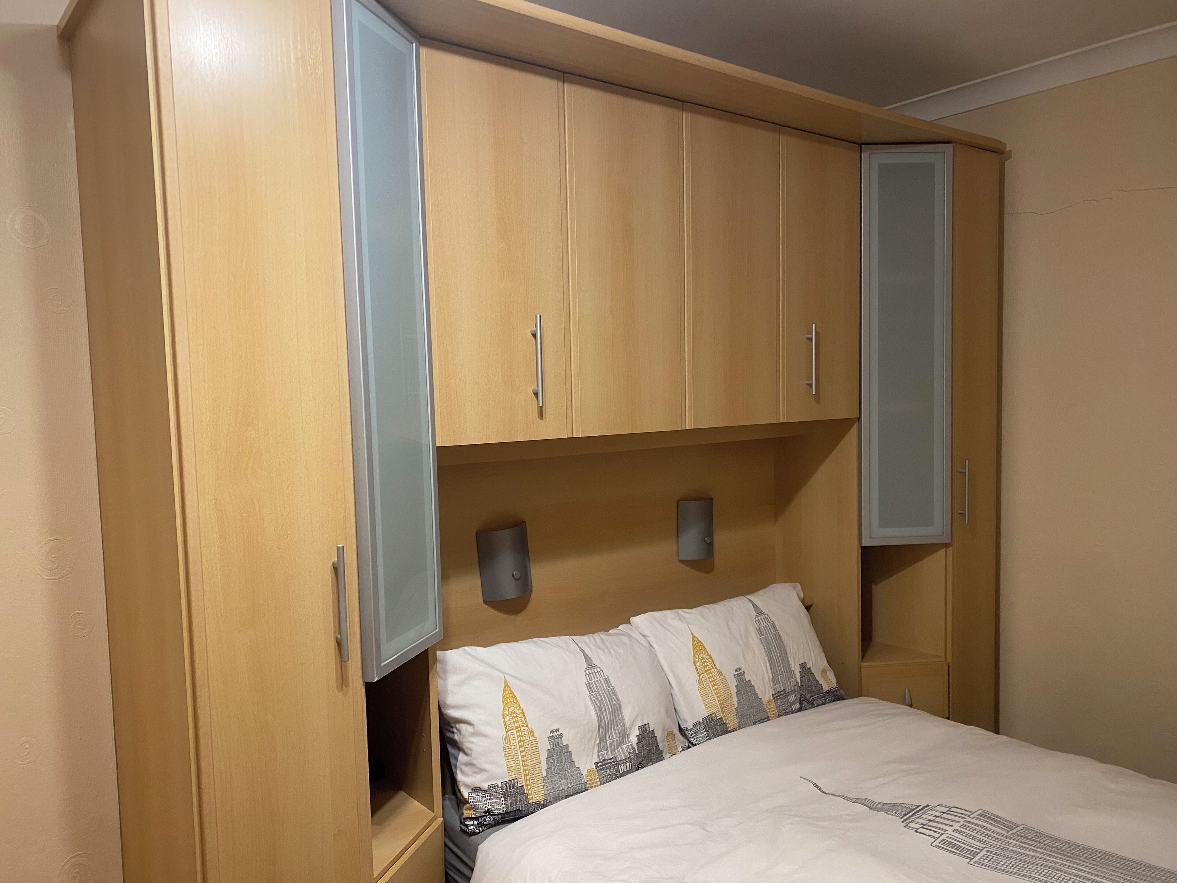 A bedroom with a bed, wooden wardrobe, and a nightstand.