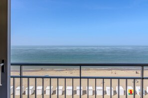 Une vue sur la plage depuis un balcon, avec des transats blancs et un ciel dégagé.