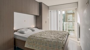 Ein modernes Schlafzimmer mit einem Bett, einem Kleiderschrank und einer Schiebetür zum Balkon.