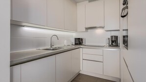 Eine moderne Küche mit weißen Schränken, einer Edelstahlspüle, einer Mikrowelle und einer Kaffeemaschine.