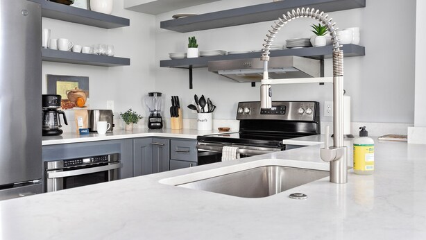 Une cuisine moderne dotée d’appareils électroménagers en acier inoxydable, de meubles de rangement gris et d’un robinet au design incurvé original.