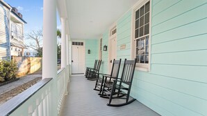 Une véranda avec des fauteuils à bascule, une porte blanche et un mur extérieur de couleur bleu clair.