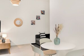 Un salón moderno con una mesa redonda, sillas blancas, un sofá gris, un cojín a rayas negras y blancas y una obra de arte en la pared.