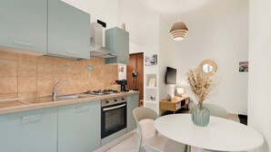 A modern kitchen with light blue cabinets, a gas stove, and an oven. There is a white dining table with chairs and a vase of dried flowers.