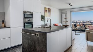 A modern kitchen with a central island, built-in ovens, and a large window offering a city view. - 1 bedroom accommodation in Sint-Idesbald (Sint-Idesbald)