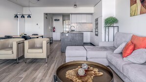 A modern living room with a grey sofa, a dining area with a wooden table, and a kitchen area with white cabinets. - 1 bedroom accommodation in Sint-Idesbald (Sint-Idesbald)