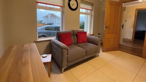 A living room with a sofa, a wooden table, and a clock on the wall. - 4bedroom House-letterkenny-privategarden-sleeps 7 (Letterkenny)