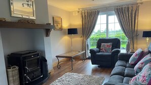 A living room with a fireplace, a sofa, a chair, and a large window with curtains. - 4bedroom House-letterkenny-privategarden-sleeps 7 (Letterkenny)