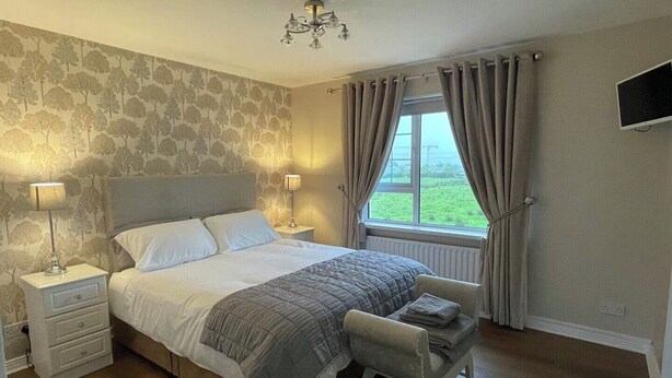 A bedroom with a bed, bedside tables, a chair, a window with curtains, and a chandelier. - 4bedroom House-letterkenny-privategarden-sleeps 7 (Letterkenny)