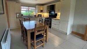 A modern kitchen with white cabinets, a dining table with chairs, and a view of greenery outside. - 4bedroom House-letterkenny-privategarden-sleeps 7 (Letterkenny)
