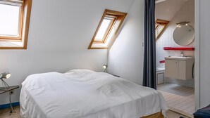 A bedroom with a bed, a bedside lamp, a window, and a view into the bathroom. - Peter Pan 97/0201 + G* / (Sint Idesbald)