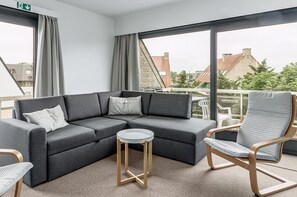 Ein modernes Wohnzimmer mit einem grauen Ecksofa, einem runden Holztisch und einem grau gepolsterten Sessel.