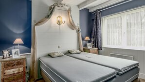 Quarto com duas camas, mesa de cabeceira com abajur, cômoda e dossel decorativo.