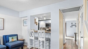 A modern living room with a blue sofa, white chairs, and a kitchen area with white cabinets and a microwave. - Porcher Villas 3 - Near Ocean! (Myrtle Beach)