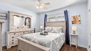 A bedroom with a bed, dresser, mirror, ceiling fan, and artwork on the wall. - Porcher Villas 3 - Near Ocean! (Myrtle Beach)