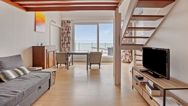 Un salon moderne avec un canapé, une table à manger et un téléviseur. Un escalier mène à un niveau supérieur.