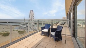 Un balcon avec deux fauteuils en osier, une rambarde en verre et une vue sur une grande roue et la plage.