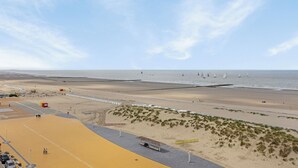 Une plage avec une zone de sable, une promenade et des voiliers visibles au loin.