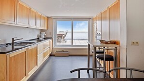 Une cuisine moderne avec des meubles en bois, un plan de travail noir et une vue sur l’extérieur grâce à une grande fenêtre.
