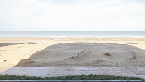 Una playa arenosa con una valla y un sendero que lleva al agua.