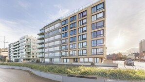 Un edificio residencial de varios pisos con balcones, una acera pavimentada y una calle con vehículos.