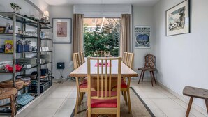 Un comedor con una mesa y sillas de madera, una estantería y vistas al exterior con vegetación.