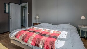 Un dormitorio con una cama grande, una mesita de noche, una lámpara y una puerta que da a otra habitación.