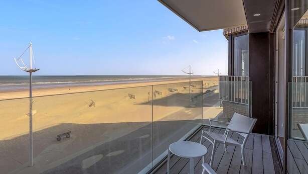 Un balcon avec vue sur la plage, comprenant une table, des chaises et un lampadaire.