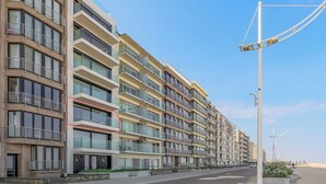 Un immeuble résidentiel à plusieurs étages, doté de balcons, donnant sur une rue et avec un ciel dégagé.