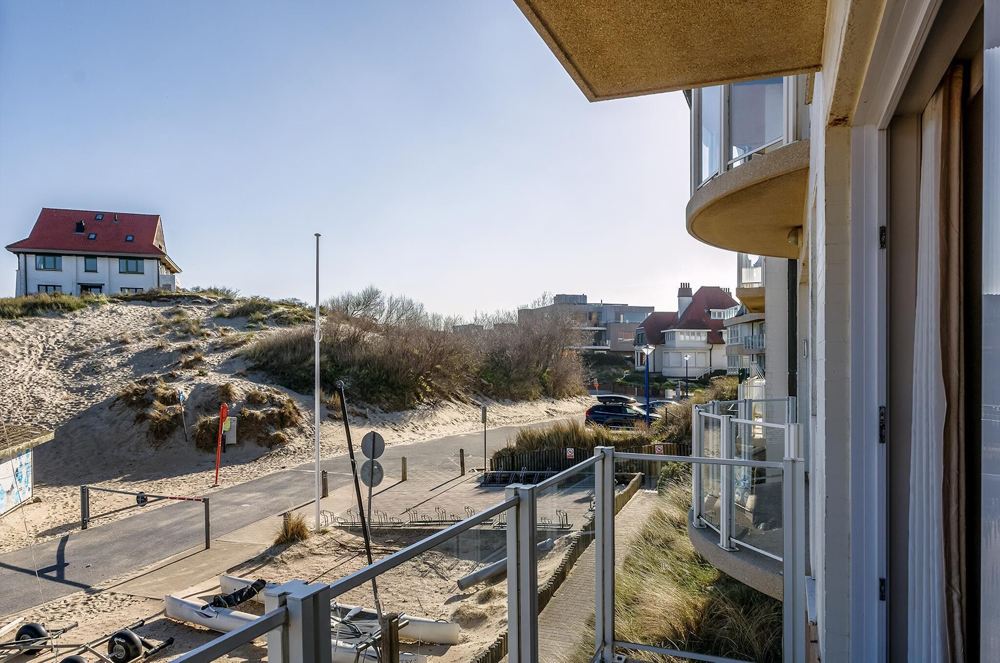 A coastal building with a red roof, a sandy beach, and a road leading to it.