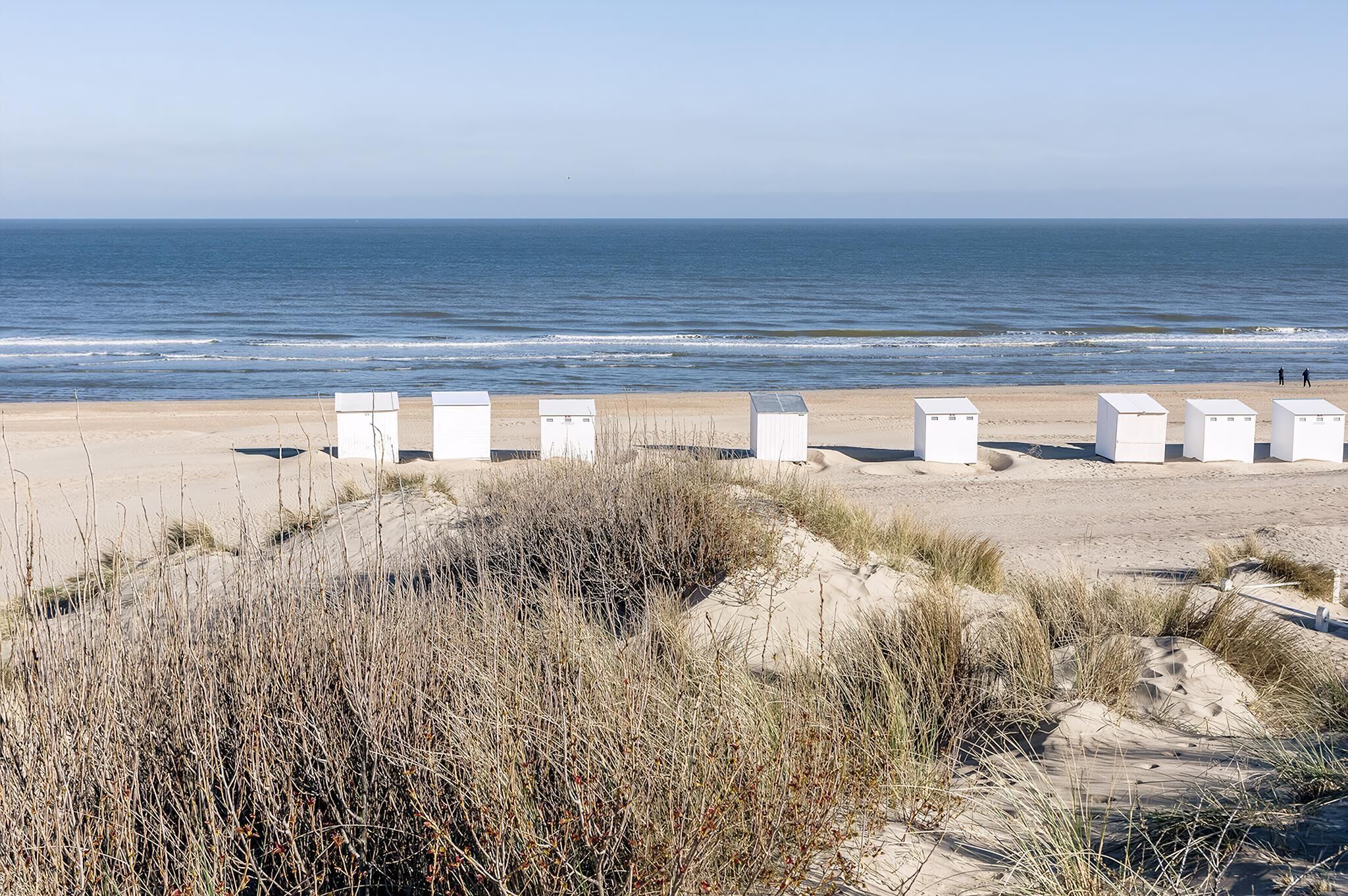 Ein Strand mit weißen Bauten, möglicherweise Strandkörben, und Dünen im Vordergrund.