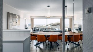 A modern dining area with a round table and orange chairs, large windows offering a view of the beach, and a minimalist decor. - 2 bedroom accommodation in Sint Idesbald (Sint Idesbald)